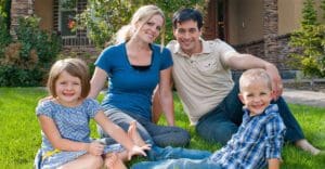 Family of 4 posing on front lawn in front of a residential home