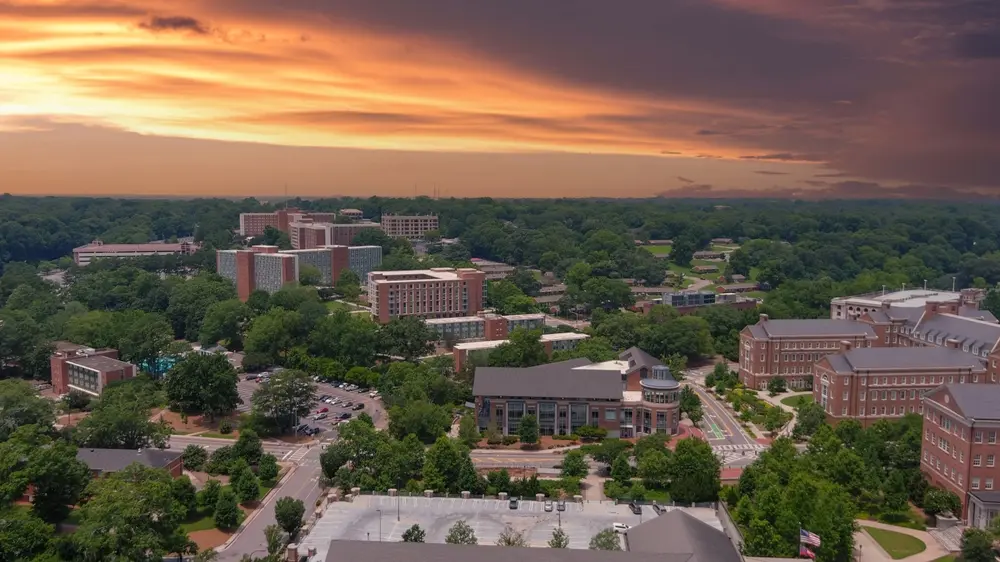 aerial shot of the red brick buildings on the campus of the University of Georgia and vast miles of lush green trees with powerful clouds at sunset in Athens Georgia USA