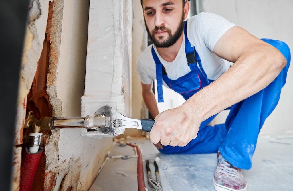 Horizontal snapshot of a plumber screwing plumbing fittings with wrench. Close-up of strong arm working with a tool during installation works in new apartment. Focus on hand with instrument.